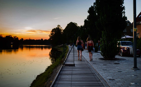 Person walking along a riverside path with city lights in the background